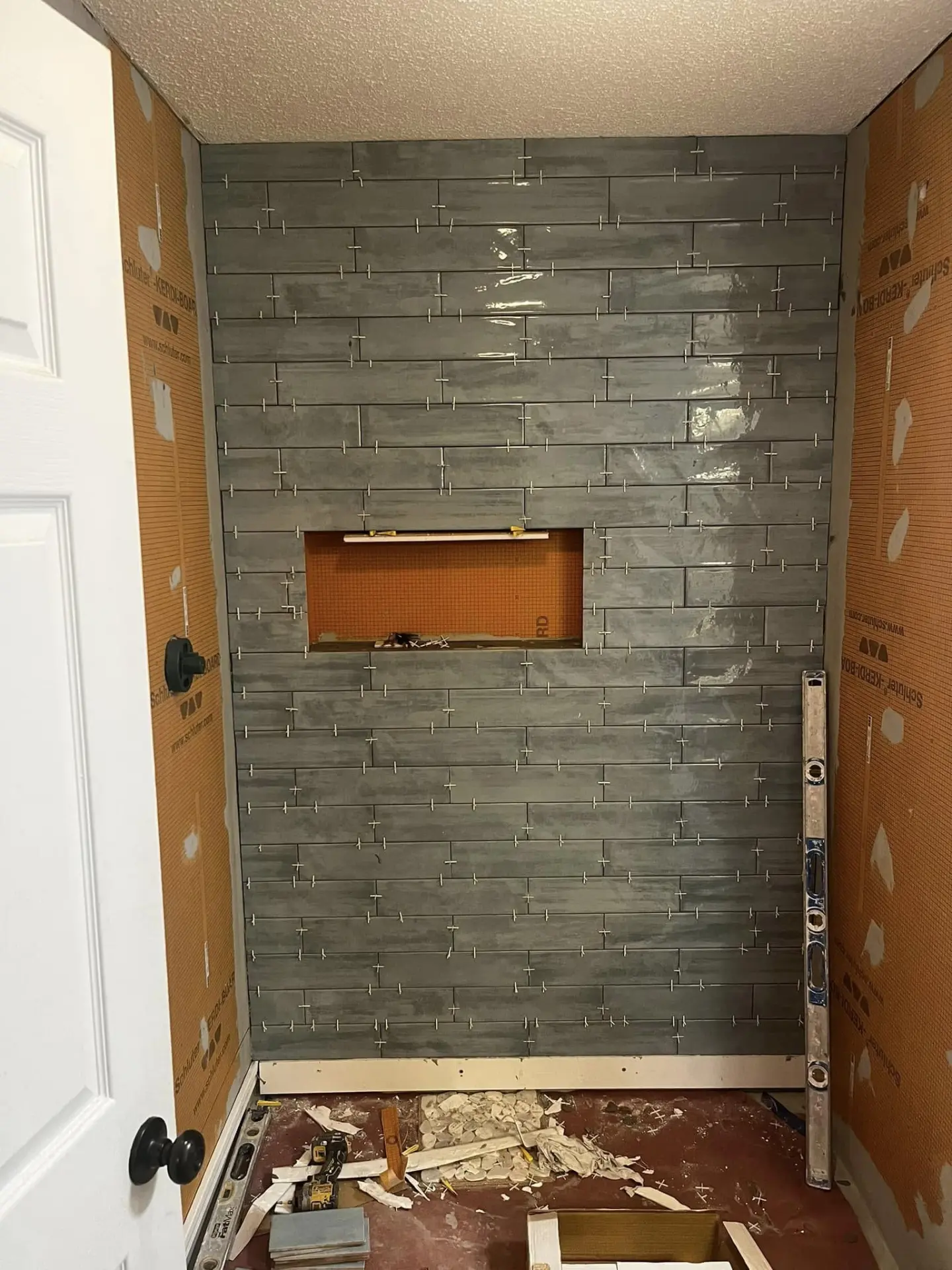 Shower wall being tiled in green subway tile over waterproof board