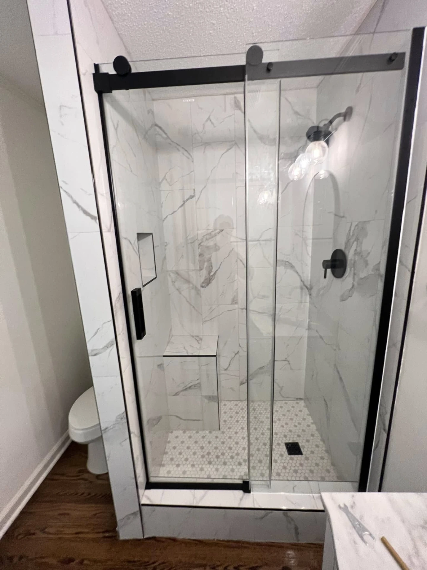 Finished walk-in shower with marble-look tile, hex mosaic floor and black glass door
