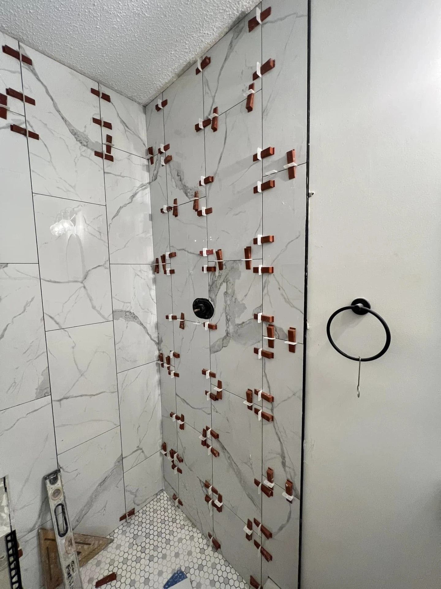 Shower walls tiled with large marble-look tile held by leveling clips