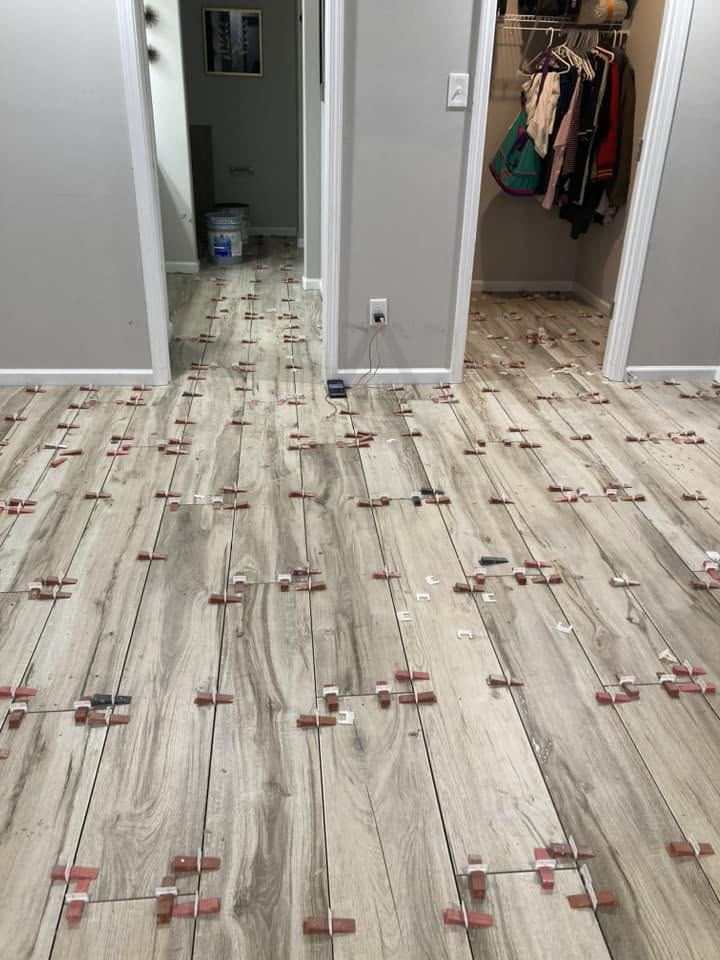 Wood-look tile floor being set with leveling clips across a bedroom and closet