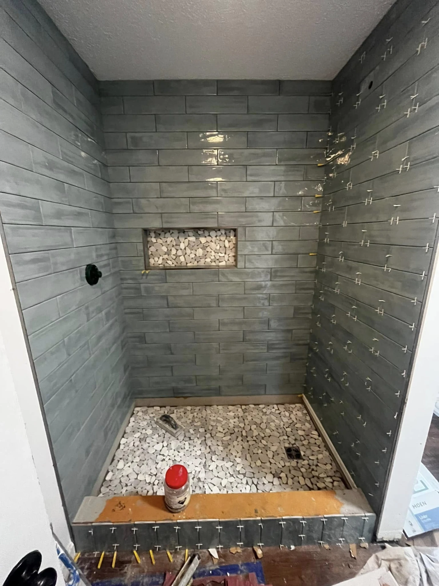 Shower tiled in green subway tile with a pebble floor and niche