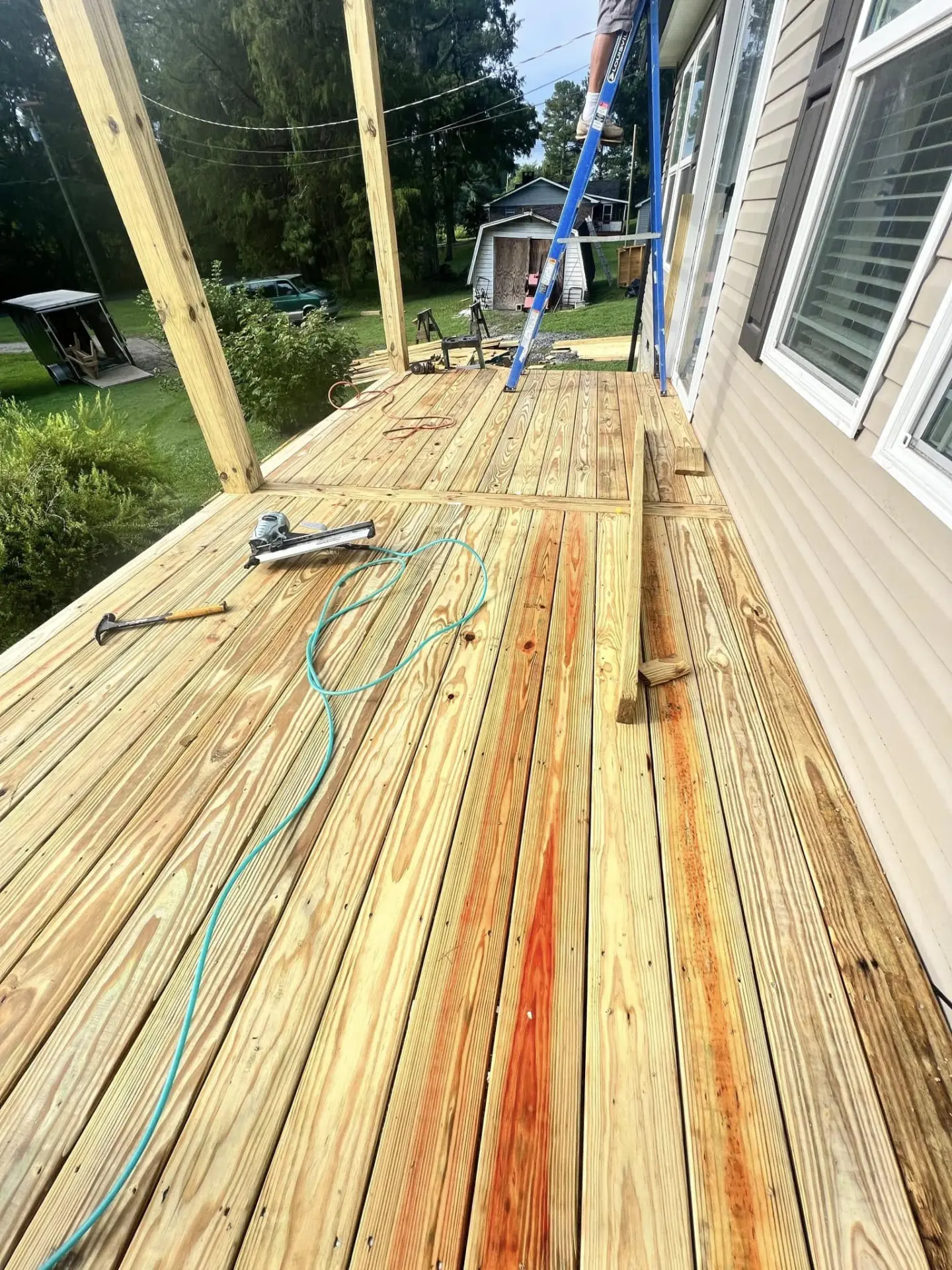 New pressure-treated deck boards being nailed down beside a house