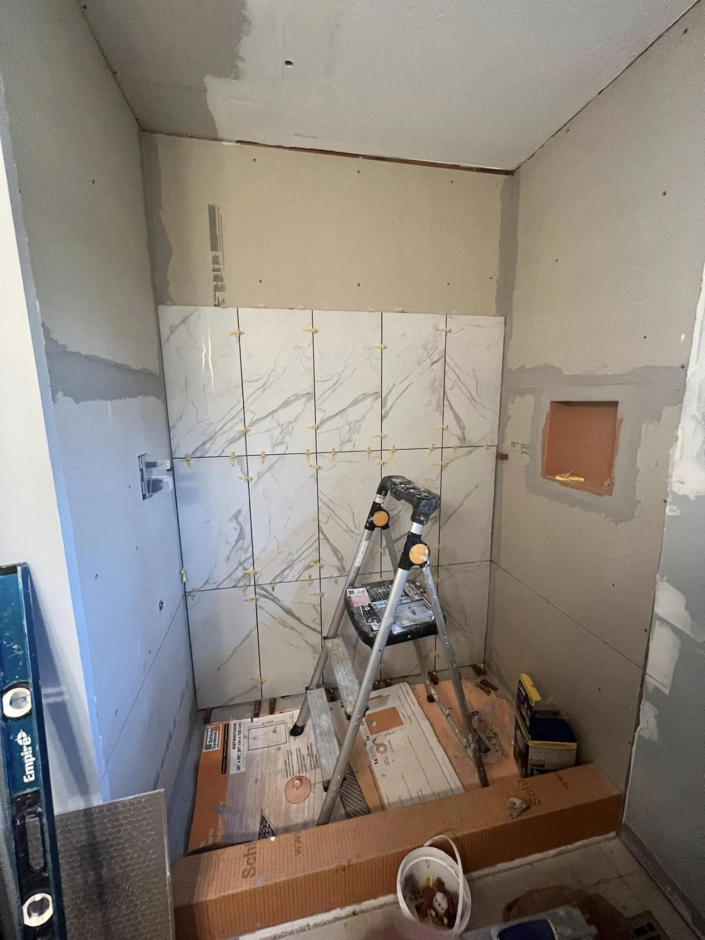 Shower wall being tiled with large marble-look tile and leveling clips
