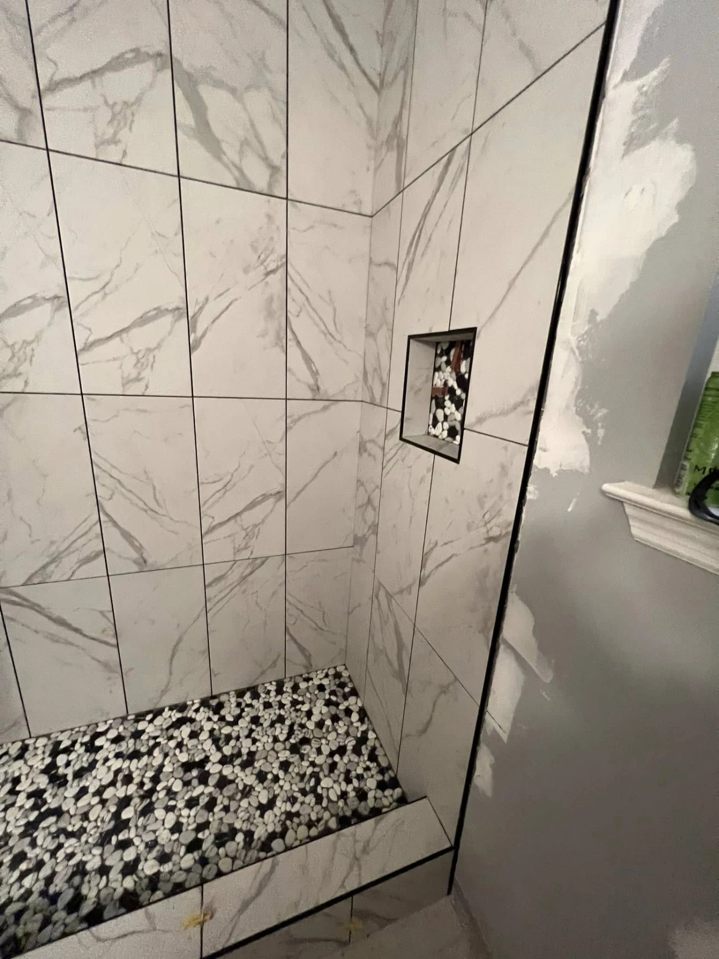 Walk-in shower with marble-look tile walls, pebble mosaic floor and built-in niche