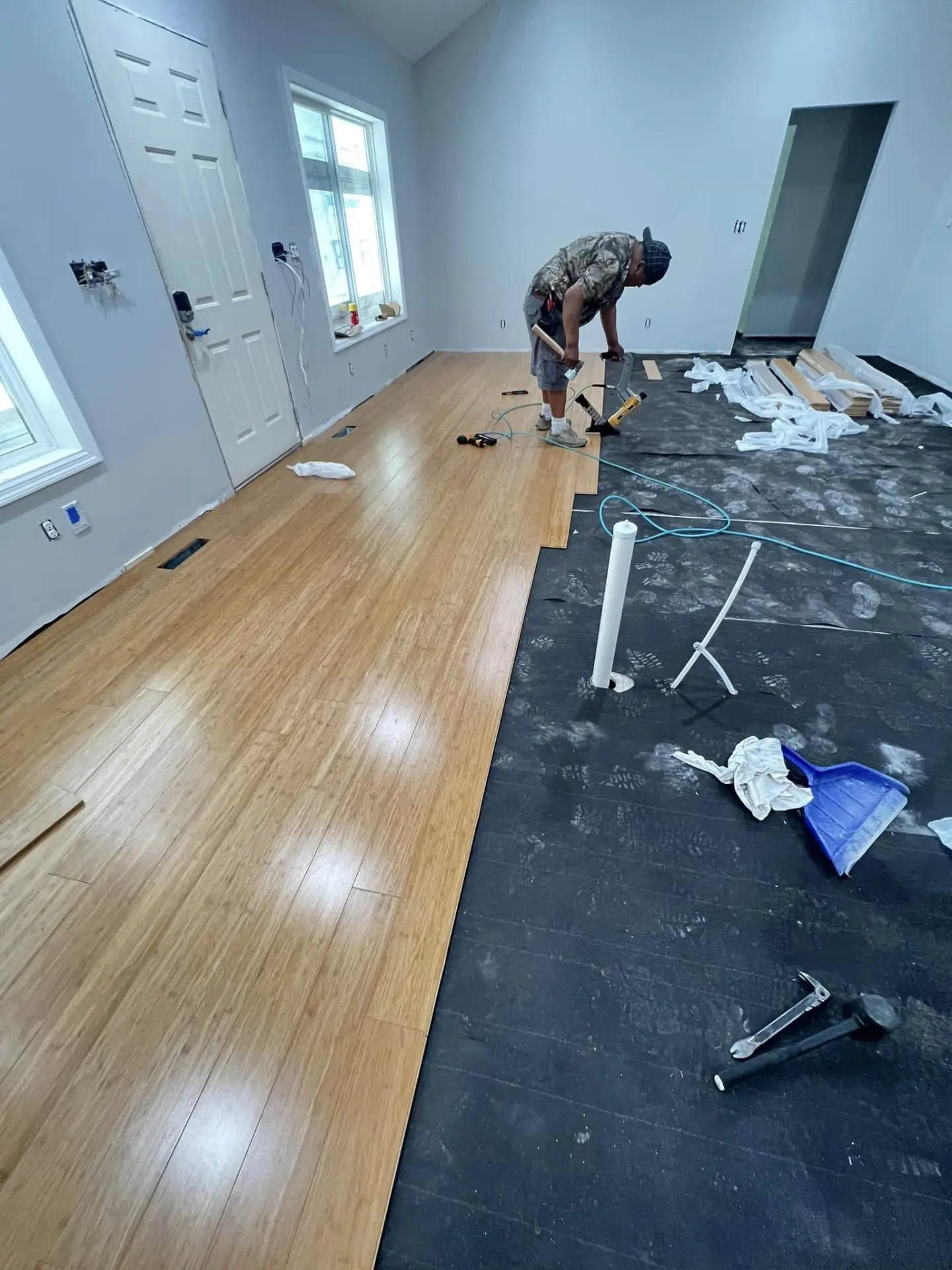 Installer nailing down hardwood planks over underlayment in a bright room