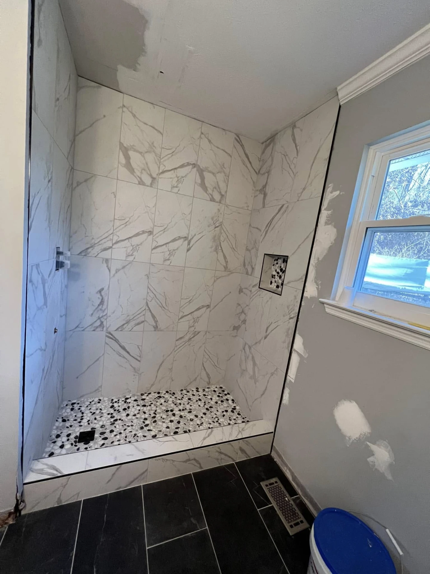 Walk-in shower with marble-look tile walls and black-and-white pebble floor